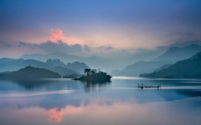 Tranquil lake with misty mountains at sunrise in Thượng Lâm, Vietnam.